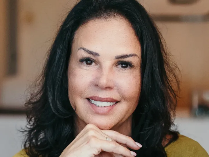 Retrato da Dra. Leila Brandão na clínica, a sorrir, com a mão apoiada no queixo